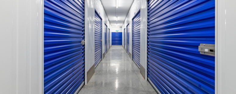 The interior of Storage King Woodley, with blue shutter door lockers on either side of a long hallway