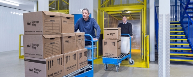 Customers using Storage King's free on-site trolleys to move heavy boxes into their storage unit.