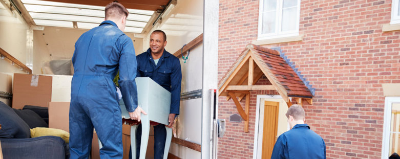 Two movers in blue overalls packing furnture into a moving van