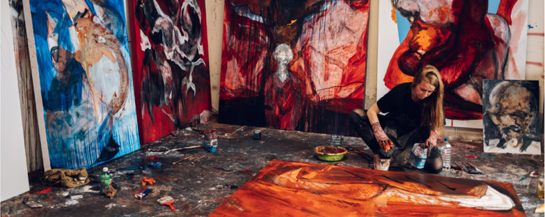 An artist working on a painting in a messy art studio